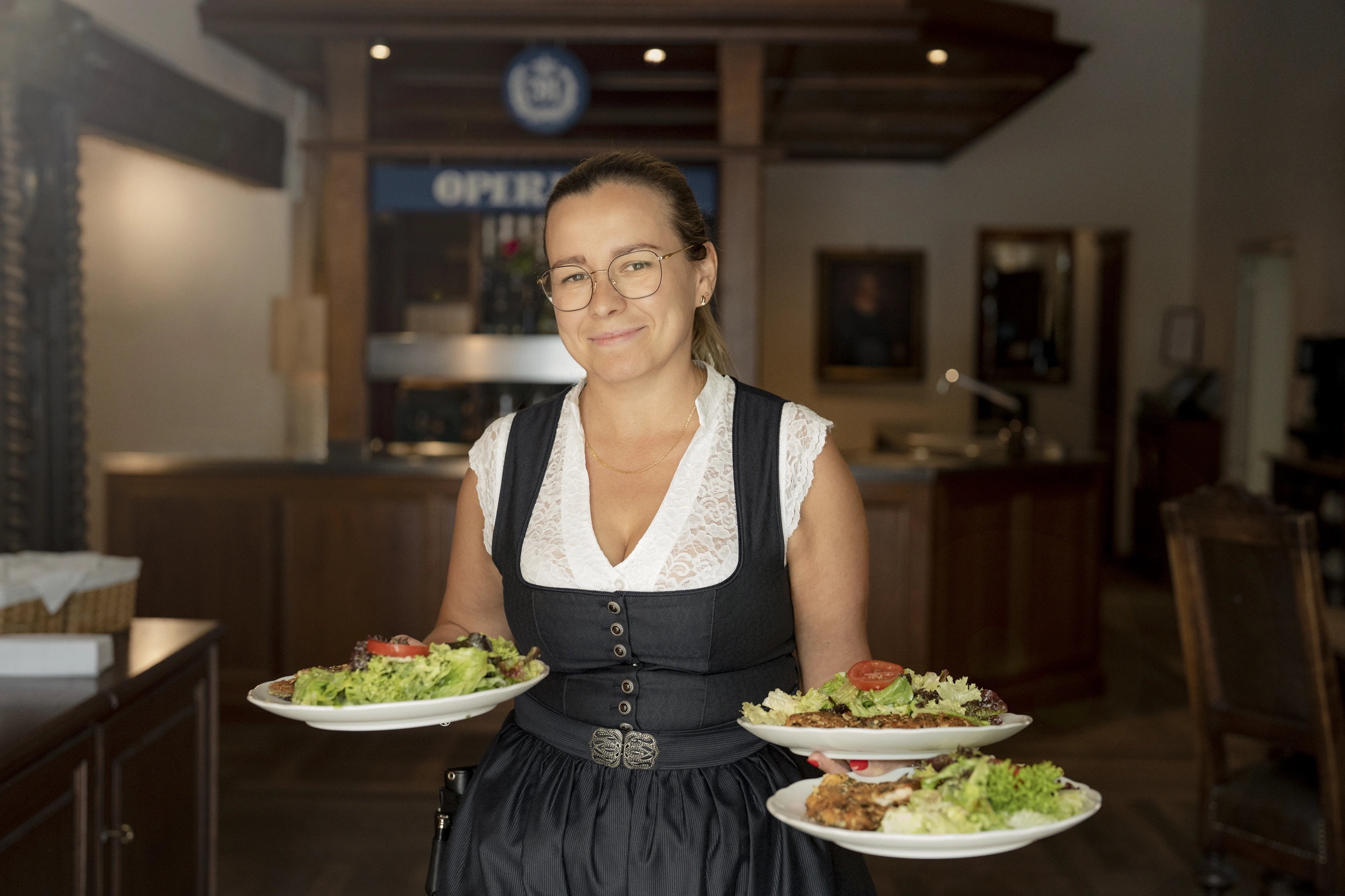 Waitress in a dirndl serving three plates with salad in the restaurant