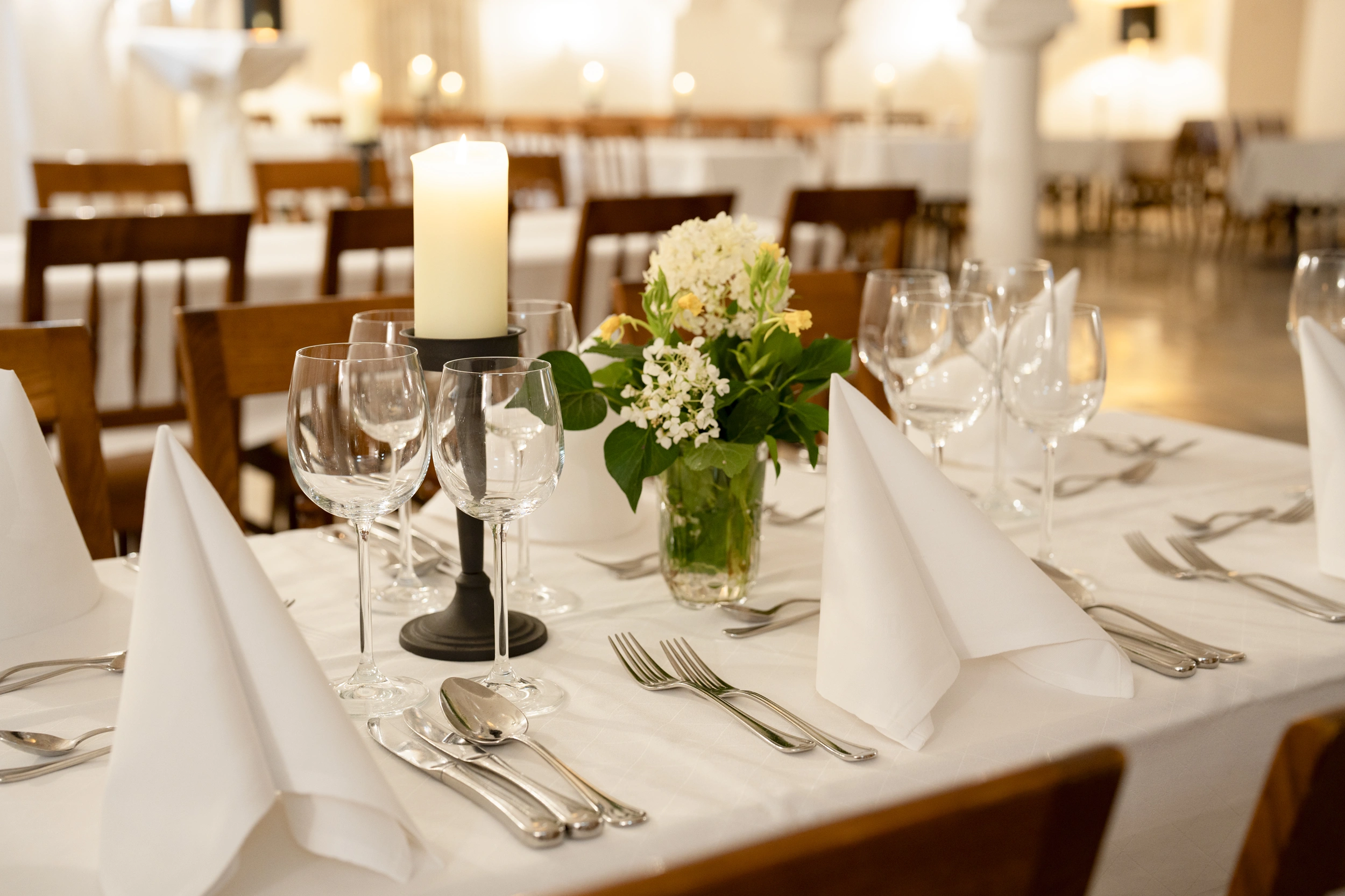 Festlich gedeckter Tisch mit Blumen, Kerze, Weingläsern und weißen Servietten.