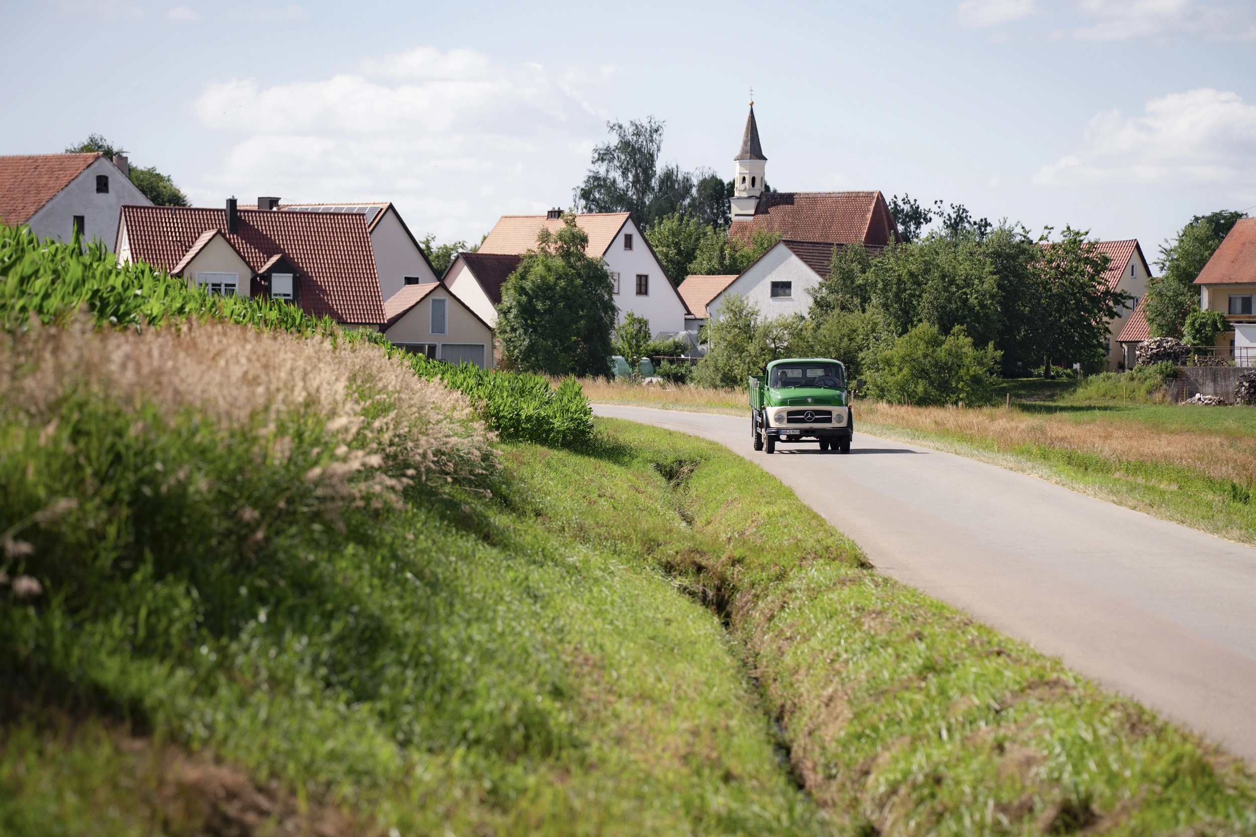 Green vintage Schlossbrauerei truck on a country road, village with church tower in the background