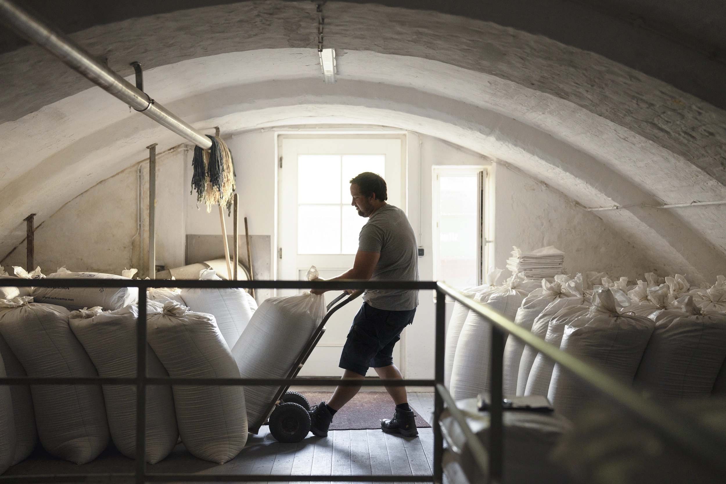 Brewer moving sacks of malt with a hand truck through the vaulted room