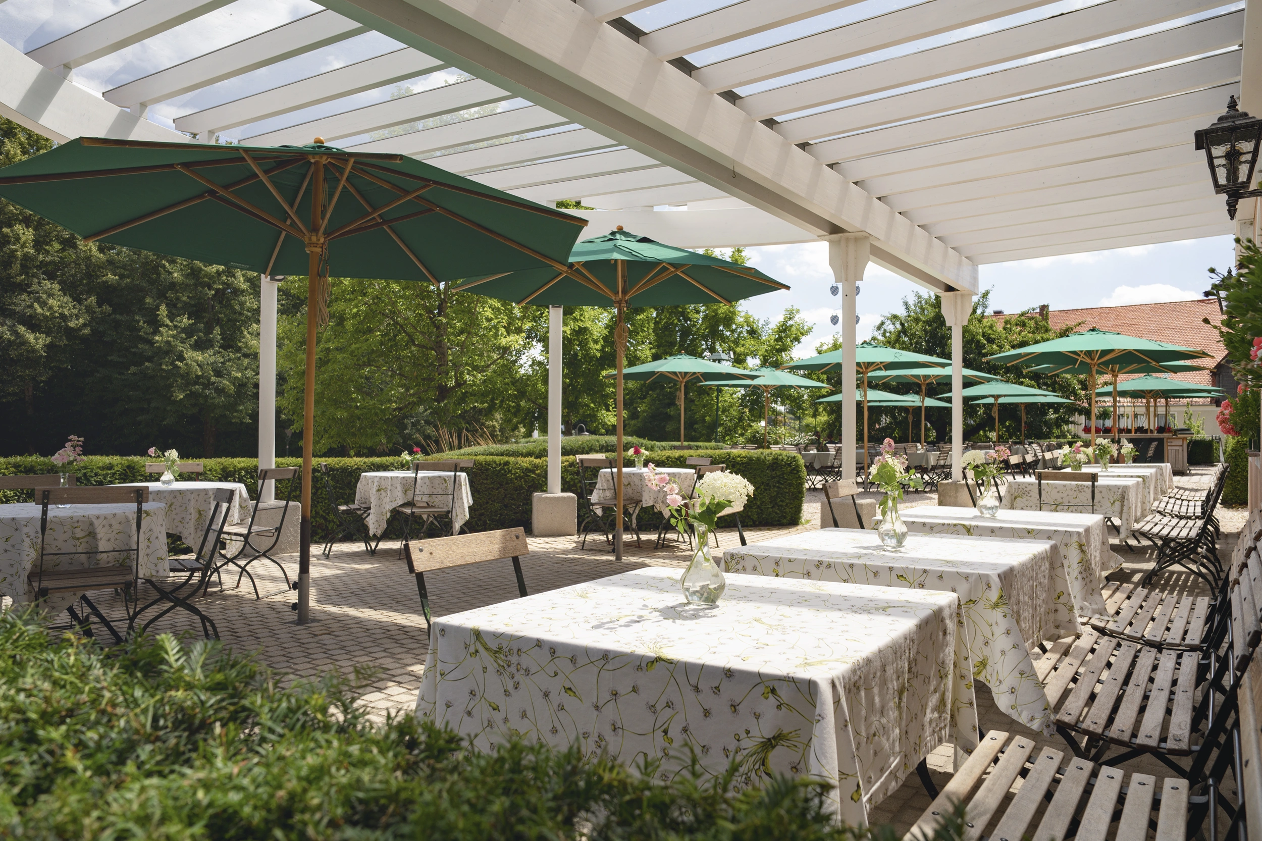 Biergarten mit gedeckten Tischen unter Pergola und grünen Sonnenschirmen