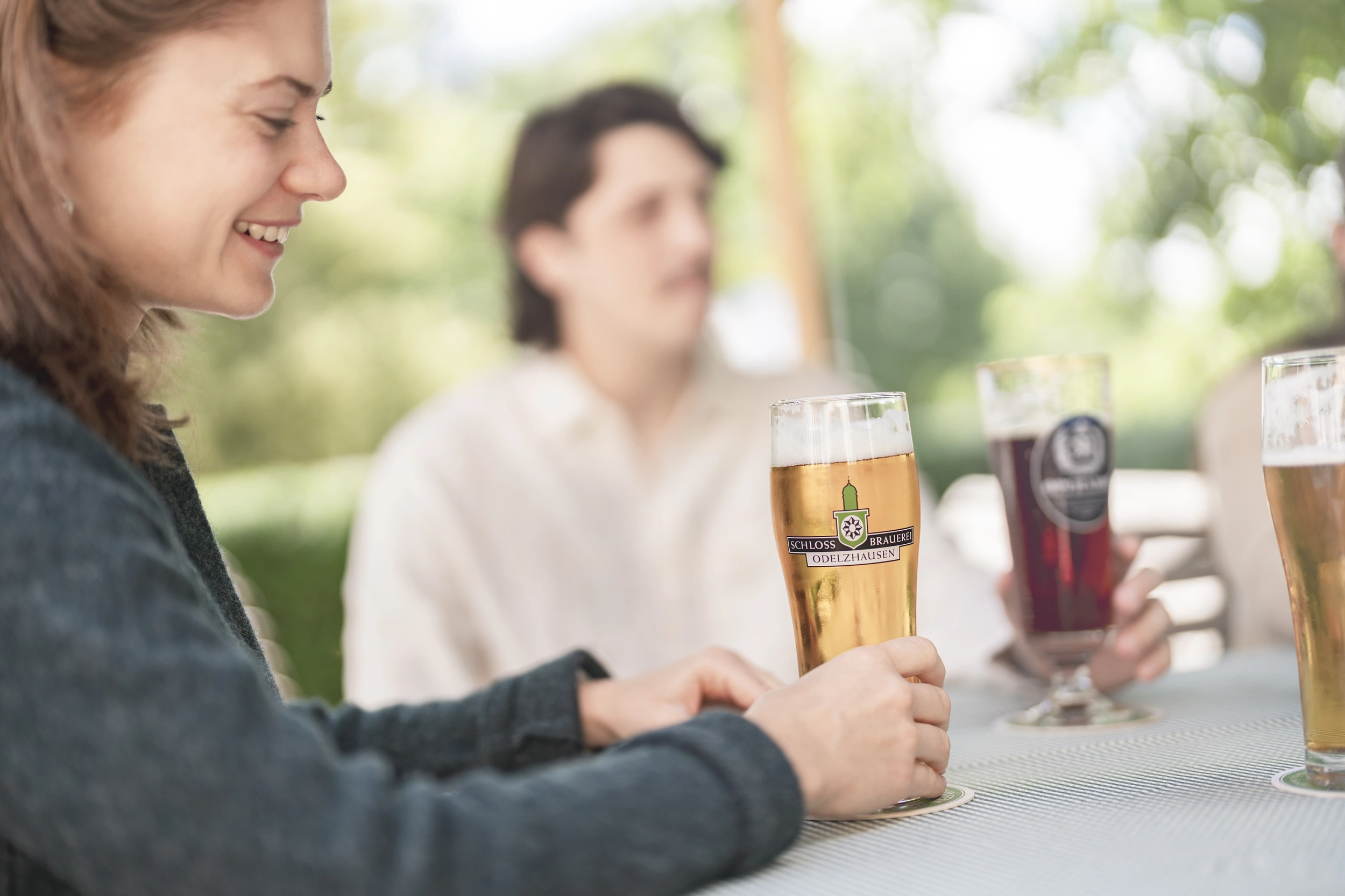 Lächelnde Frau mit einem Glas Hellem der Schlossbrauerei im Biergarten